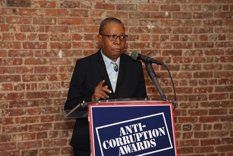 A person in a suit and tie in front of a brick buildingDescription automatically generated