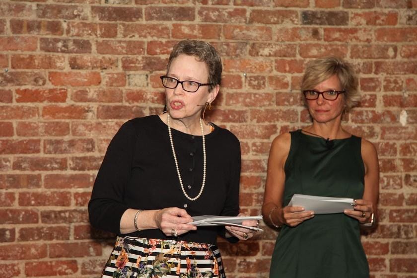 Two people standing in front of a brick wallDescription automatically generated